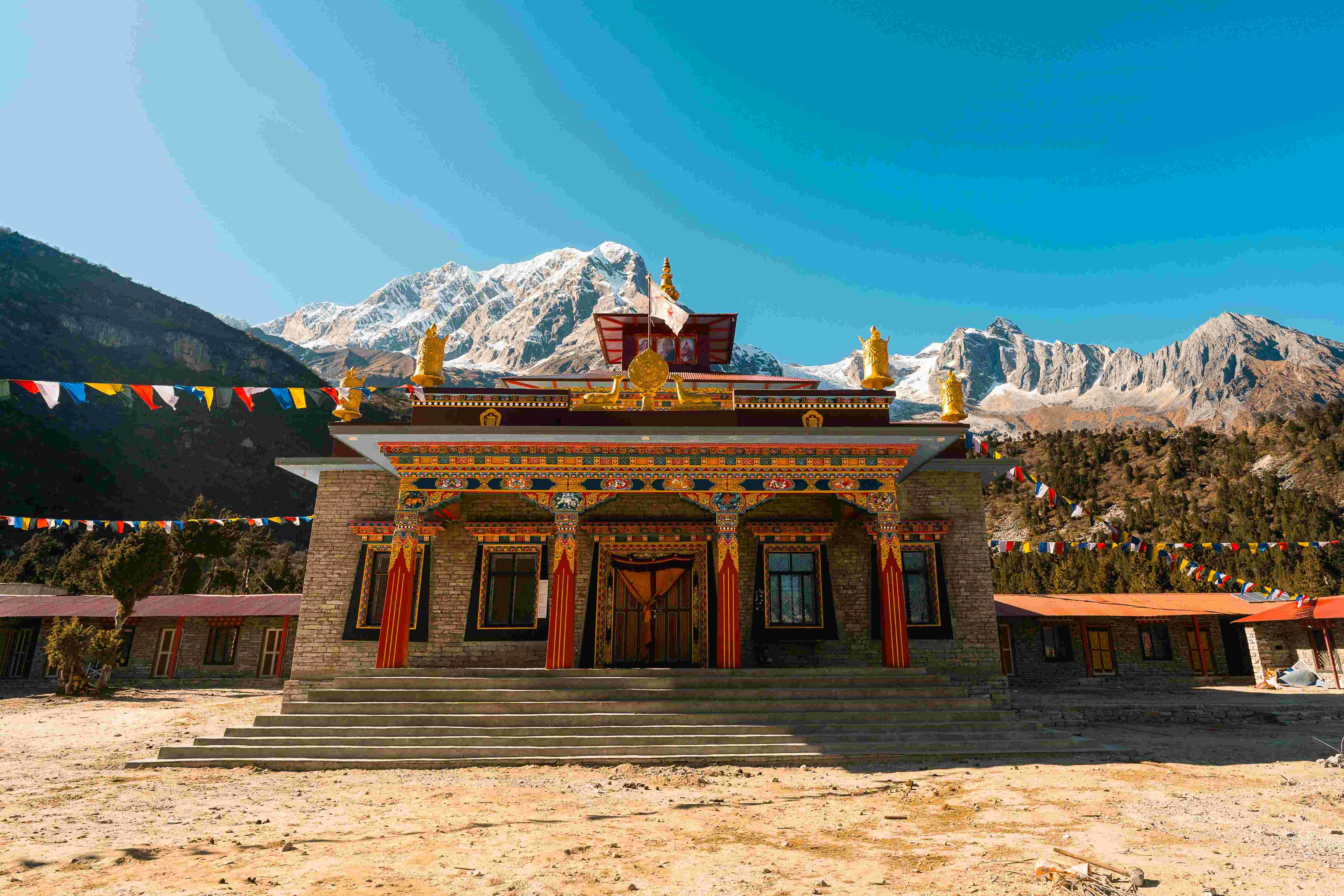 Beautifully architectures Buddhist monastery in Samagaon village with mountain peaks behind under a blue sky.