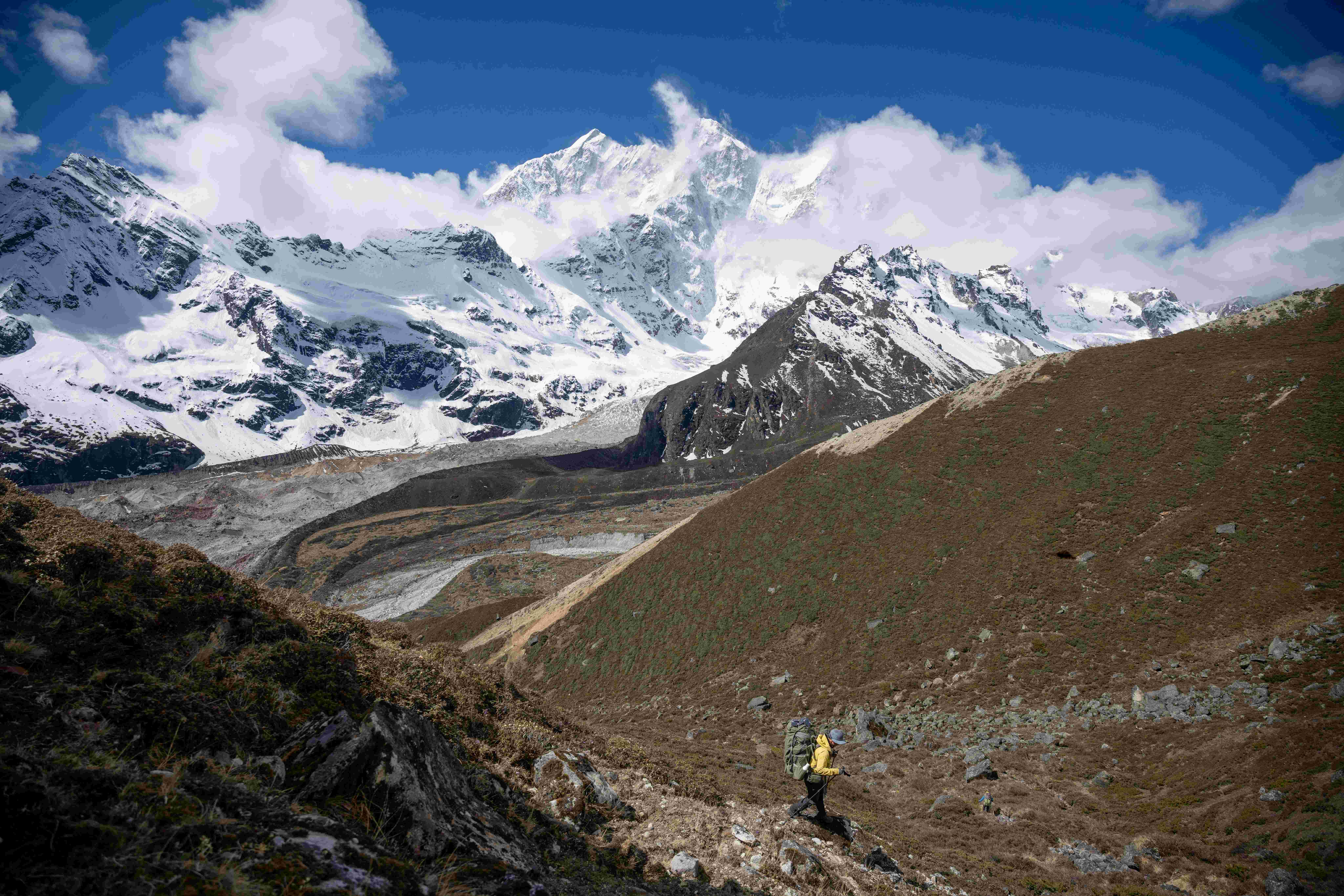 trekker with a backpack walking on a mountain trail towards a massive snow-covered peak on Manaslu trek.