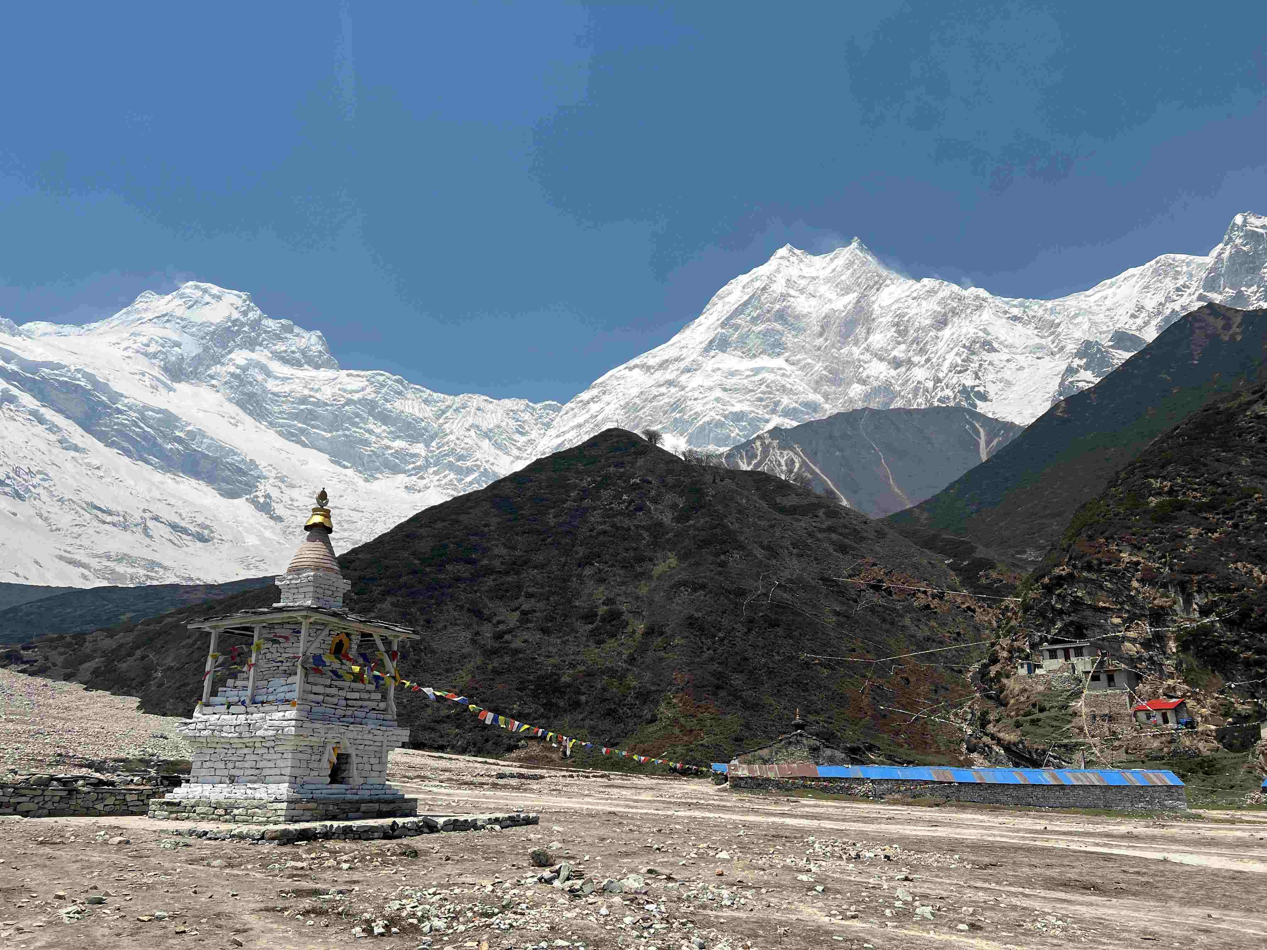 Traditional Buddhist chorten decorated with prayer flags against snow-capped peaks of Mount Manaslu.