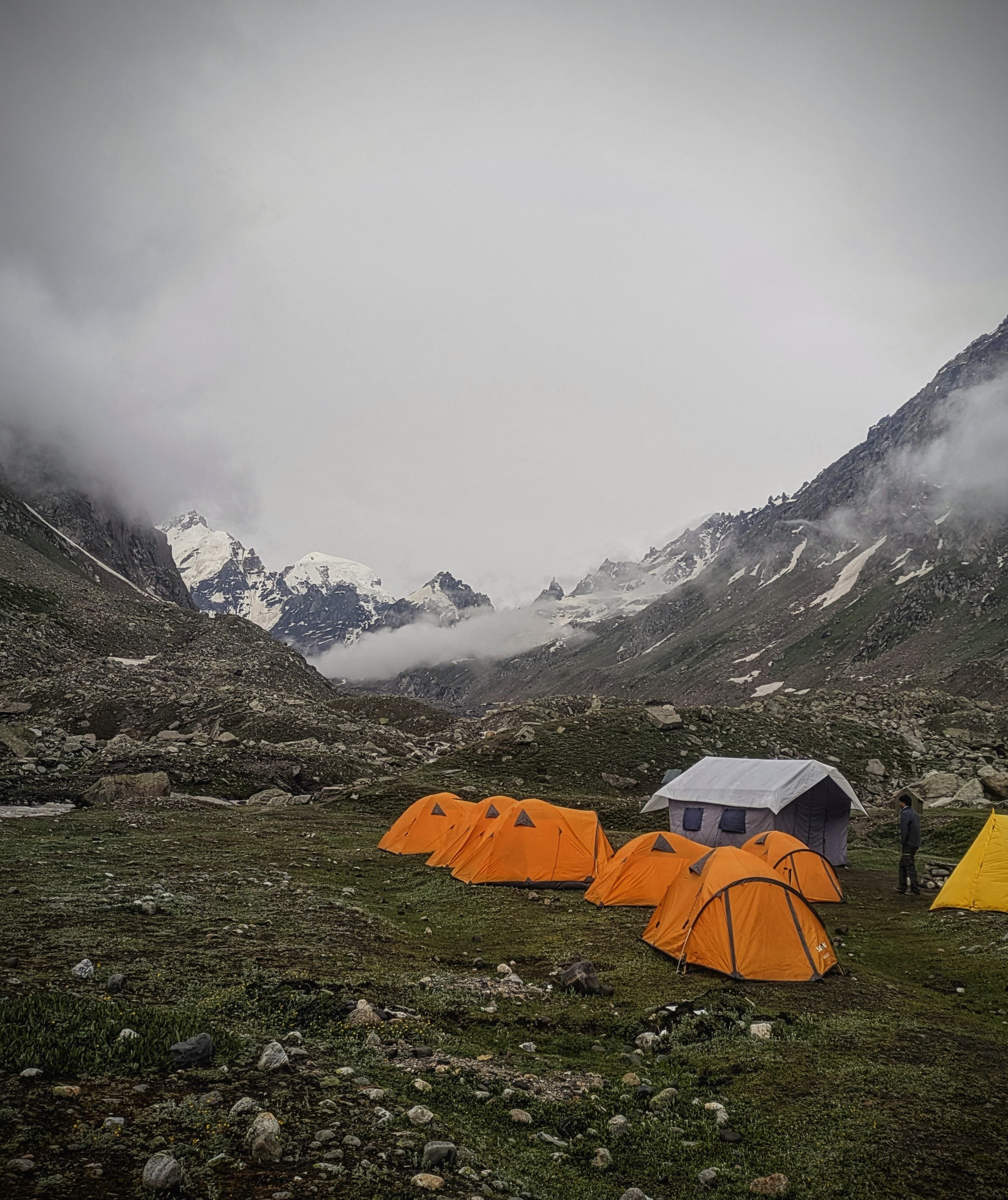 Vibrant orange camping tents set up at a scenic base camp during the Hampta Pass expedition.