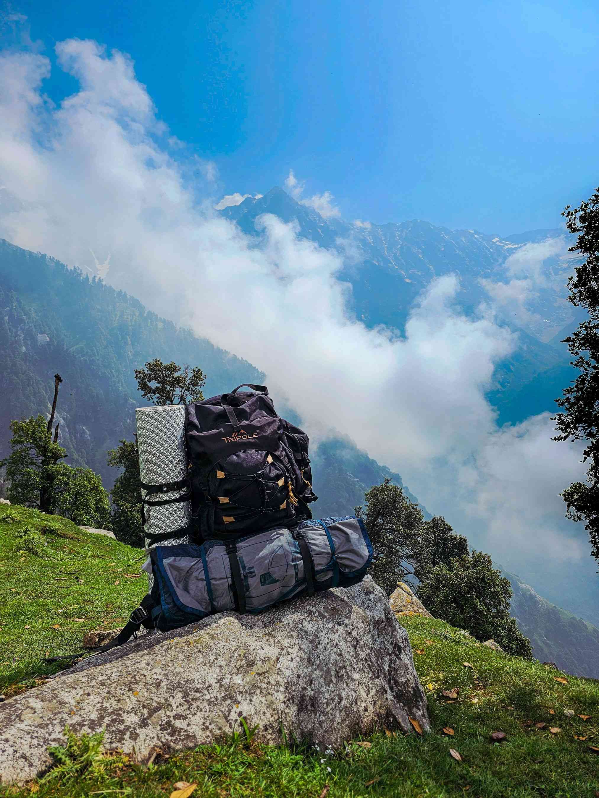 A professional trekking backpack with a sleeping mat sitting on a rock overlooking the Hampta Pass mountains.